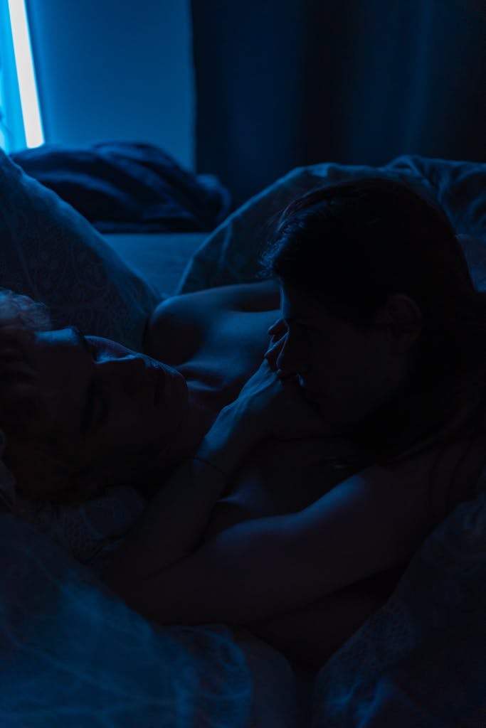 A romantic embrace between two adults in a dark, ambient bedroom setting. Perfect for themes of love and intimacy.