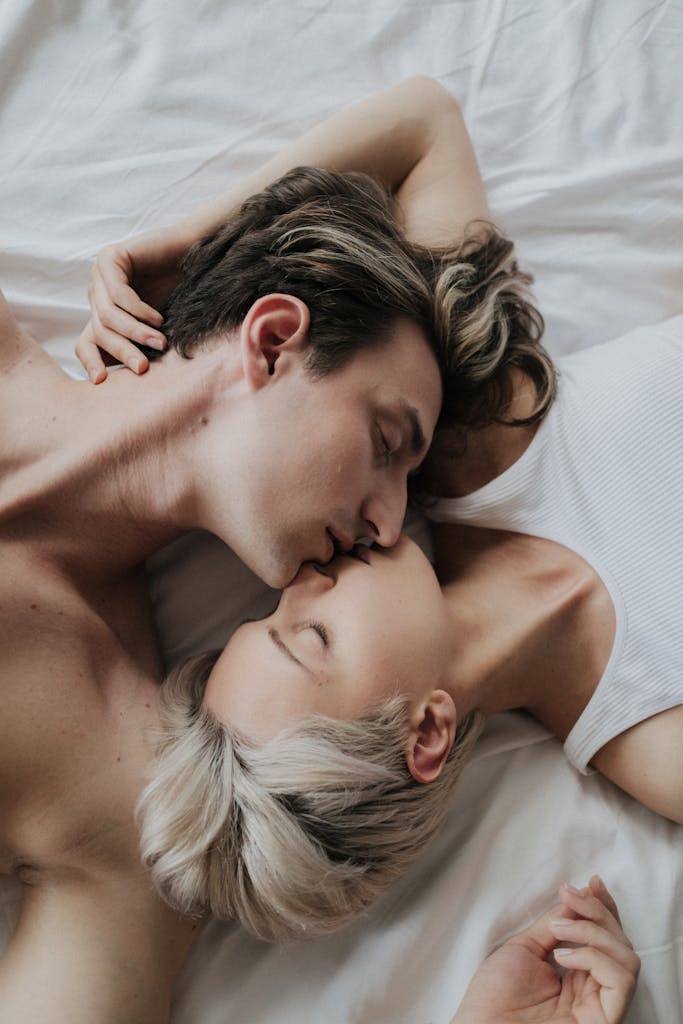 Romantic couple sharing a tender moment while lying on a white bed, showcasing love and intimacy.